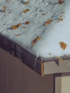Homeowner checks a residential roof with binoculars while clean gutters and early snow appear around the house.